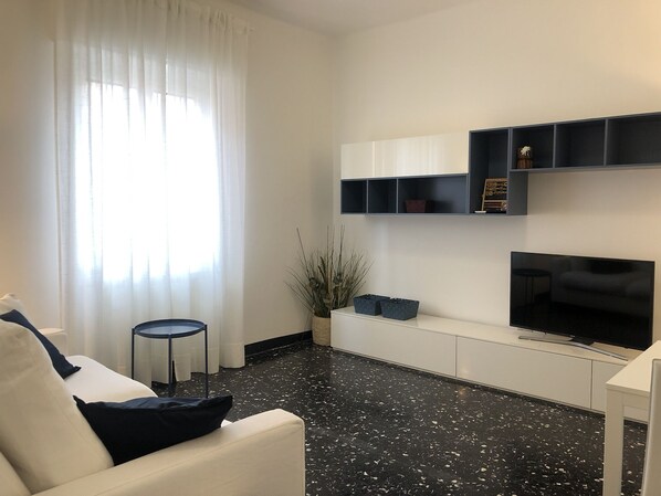 A modern living room with a white sofa, a black-framed TV, and a black and white speckled floor.