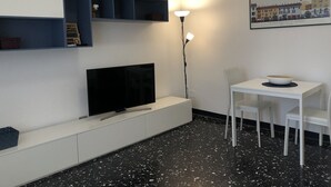 A modern living room with a flat-screen TV, a white dining table with a bowl, and a floor lamp.