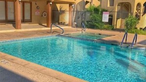Piscina com água azul cristalina, cercada por um edifício com fachada bege e palmeiras.