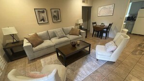 Uma sala de estar com sofá, poltronas, mesa de centro e um espaço de jantar com mesa e cadeiras.