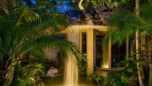 Une cascade artificielle agrémentée d’une structure en pierre et entourée d’une végétation luxuriante.