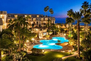 A resort with a large pool, palm trees, and a building with multiple windows. - Ocean-View Condo at North Coast Village | B222 (Oceanside)