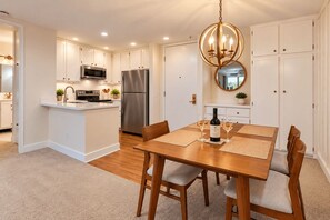 Una cocina moderna con armarios blancos, electrodomésticos de acero inoxidable y un comedor con mesa y sillas de madera.