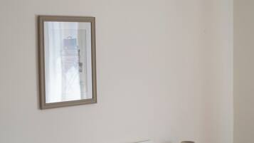 A neatly made bed with white linens and a red quilt, a bedside lamp, and a framed picture on the wall.