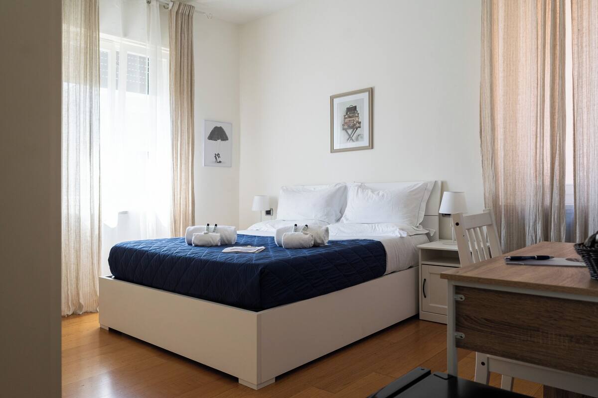 Een keurig opgemaakt slaapkamer met een bed, nachtkastjes, een bureau en een stoel.