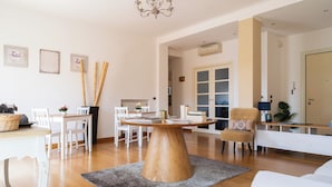 Een ruime woonkamer met een ronde houten salontafel, witte meubels en een kroonluchter.