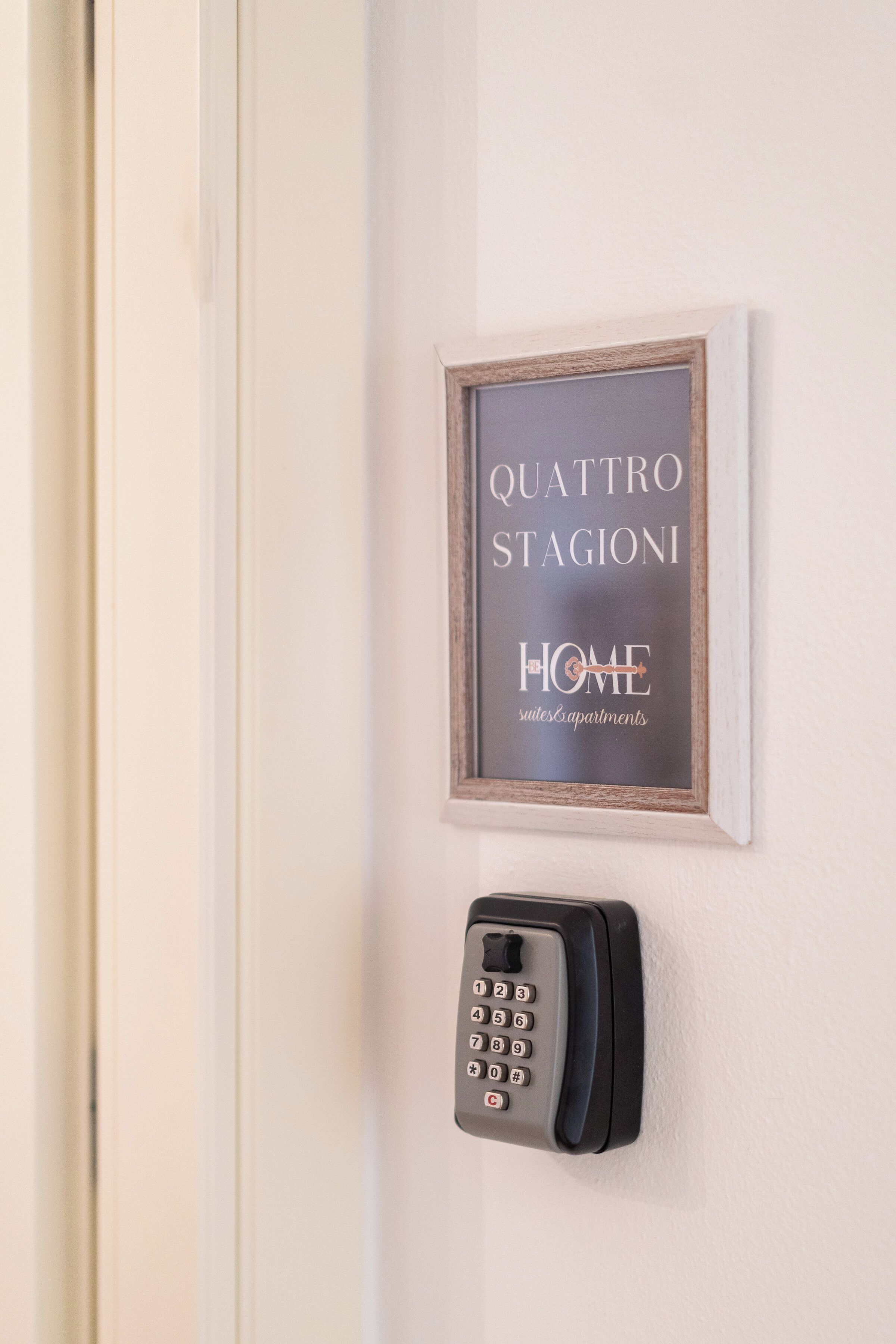 Et indrammet skilt med "QUATTRO STAGIONI HOME" og en keypadlås på en dør.