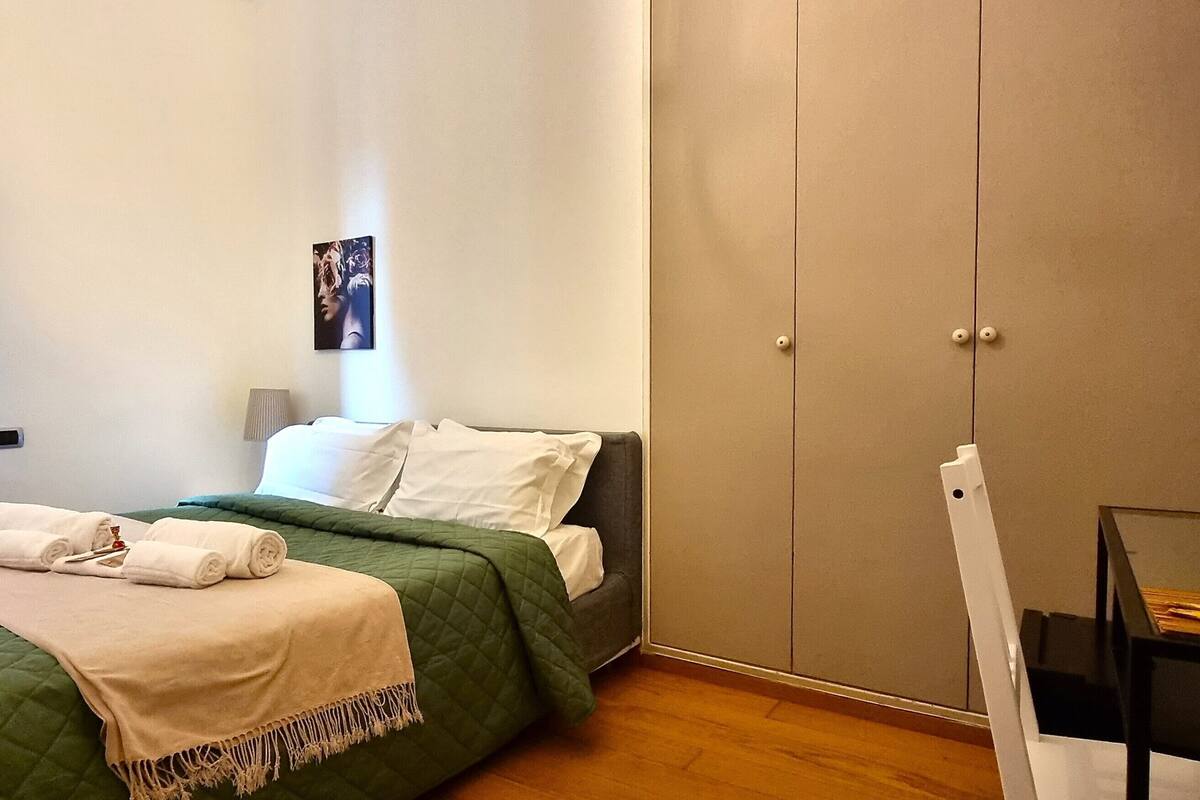 Een slaapkamer met een bed, een kledingkast, een stoel en een schilderij aan de muur.