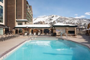 Una piscina con sillones de descanso y vistas a montañas nevadas.