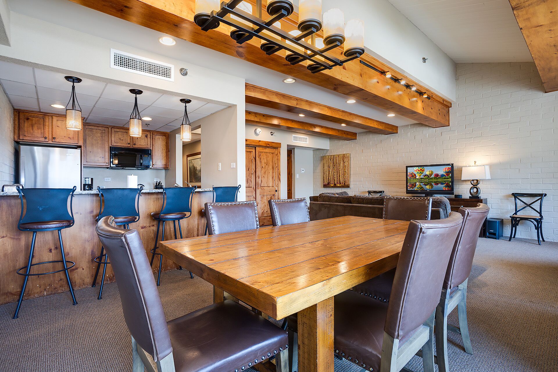 A spacious dining area with a wooden table and leather chairs, a kitchen with wooden cabinets and a stainless steel refrigerator, and a living area with a television and seating.