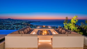 A rooftop lounge with a fire feature and a view of a cityscape at dusk.