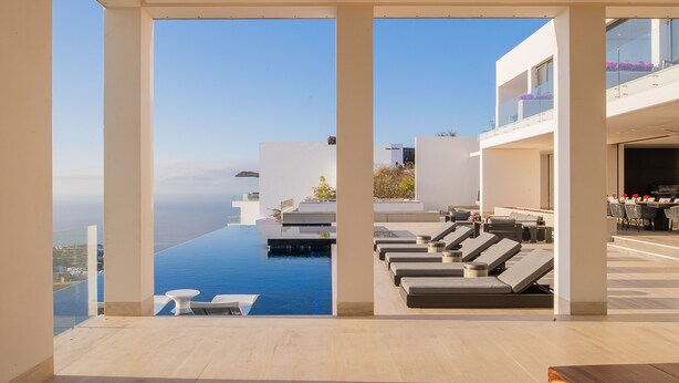 A modern outdoor lounge area with a pool, sun loungers, and a view of the ocean.