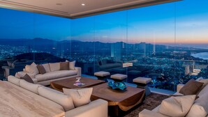 A modern living room with a panoramic city view, furnished with sofas and coffee tables, and large glass windows.