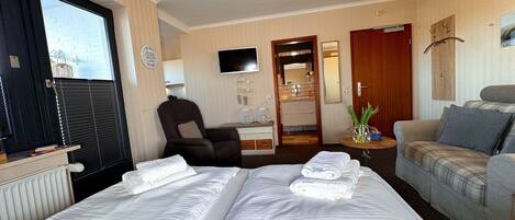 A hotel room with a bed, a chair, a sofa, a TV, and a bathroom visible through an open door.
