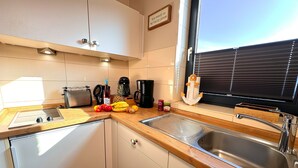 Een moderne keuken met een roestvrijstalen spoelbak, een houten aanrechtblad en witte kasten. Er staat een broodrooster, een koffiezetapparaat en een decoratieve anker op het aanrecht.