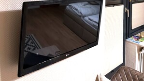 Een flatscreen televisie aan een muur bevestigd, een bed met een bedspreide met patroon, en een bordje met de tekst 'ON BEACH TIME'.