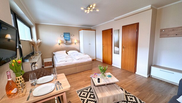Een moderne hotelkamer met een bed, een televisie, een eethoek met een gedekte tafel voor twee en een kleine salontafel.