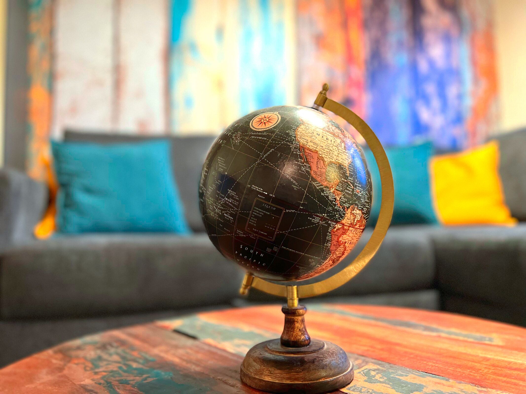 A globe on a wooden stand in a room with a colorful abstract painting in the background.