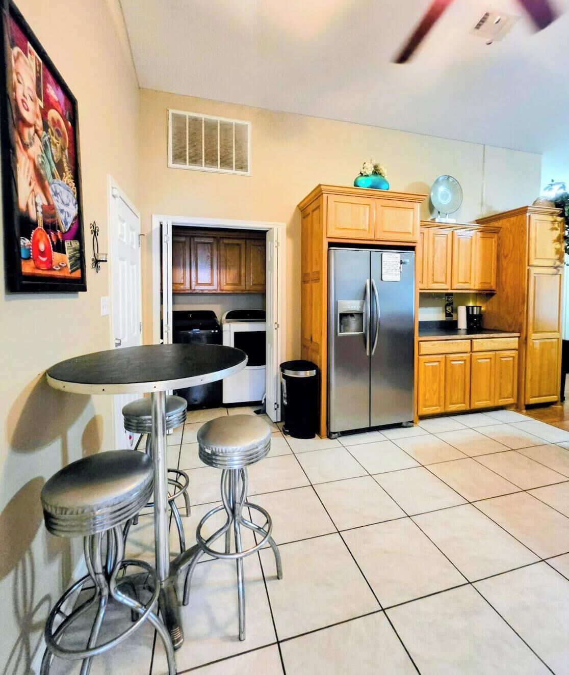A kitchen with a stainless steel refrigerator, wooden cabinets, a tiled floor, and a bar stool.