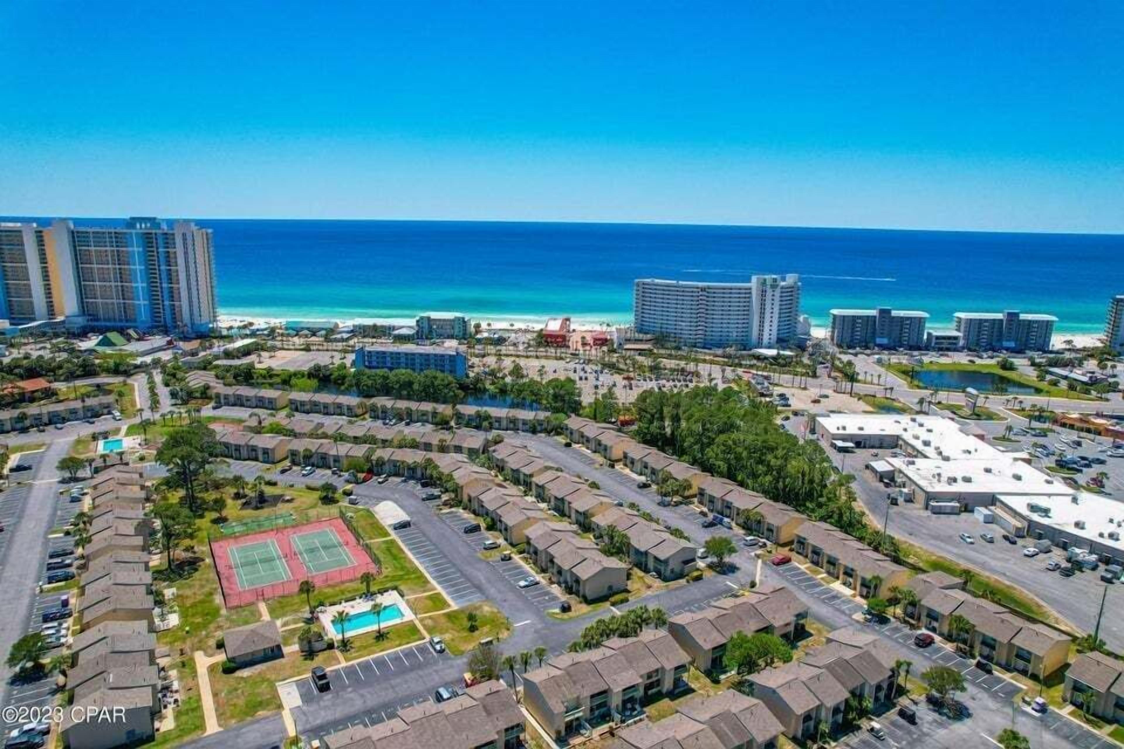 A coastal residential area with a large hotel complex, a tennis court, and a parking lot.