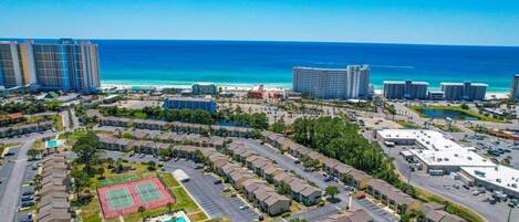 A coastal residential area with a large hotel complex, a tennis court, and a parking lot.