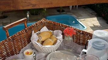 A wicker basket with breakfast items, a glass of juice, and a view of a swimming pool.