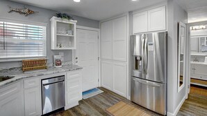 Eine moderne Küche mit weißen Schränken, einem Edelstahl-Kühlschrank, einem eingebauten Backofen und einer Kaffeemaschine auf der Arbeitsplatte.