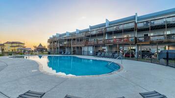 A swimming pool with lounge chairs and a multi-story building with balconies.