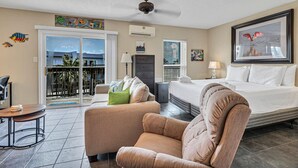 A hotel room with a bed, a chair, a desk, and a balcony with a view.