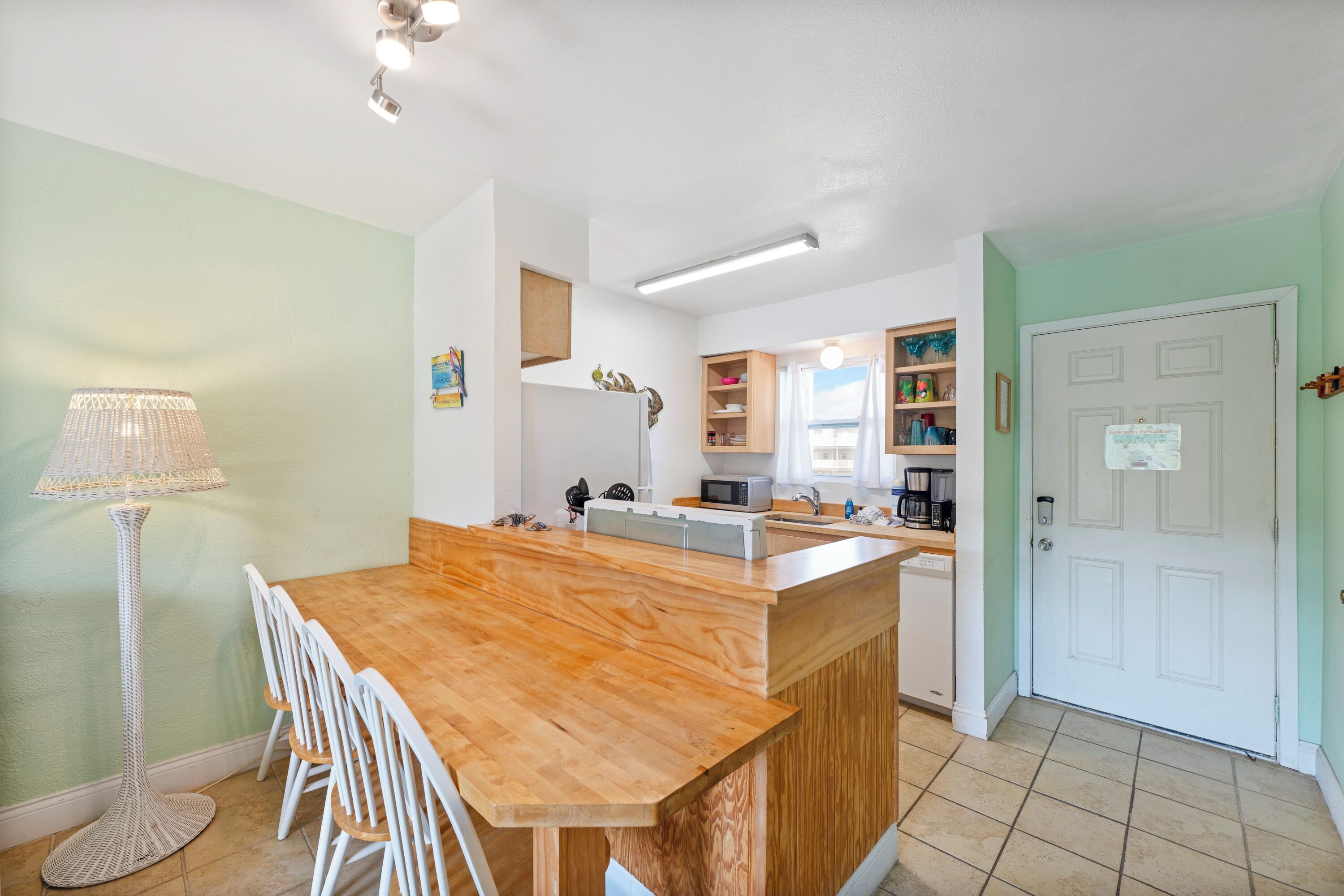 A kitchen with a wooden island, white chairs, a floor lamp, and a white door.