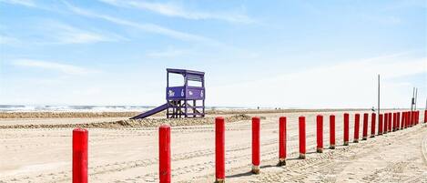 A lifeguard tower on a sandy beach with red posts lining the shore.