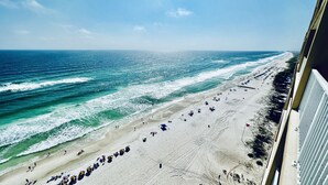 Ein Strand mit Reihen von Sonnenschirmen und Liegestühlen, freier Blick auf den Ozean und eine sandige Küstenlinie.
