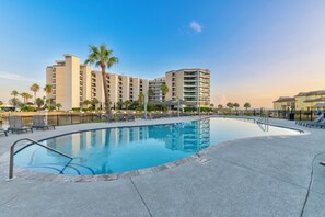 A swimming pool with lounge chairs and a palm tree, surrounded by a fence and buildings. - Spacious studio condo with the best amenities in Port Aransas! (Port Aransas)