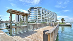 A wooden pier leading to a modern multi-story hotel with balconies, a dock, and a clear blue sky. - Spacious studio condo with the best amenities in Port Aransas!  Community pool, (Port Aransas)
