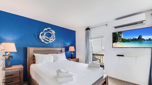 A neatly made bed with white linens and towels, a blue accent wall, a mounted TV, and a wooden nightstand with a lamp. - Top floor Bay Tree D6 condo with amazing ship channel views!  Offers ample boat (Port Aransas)