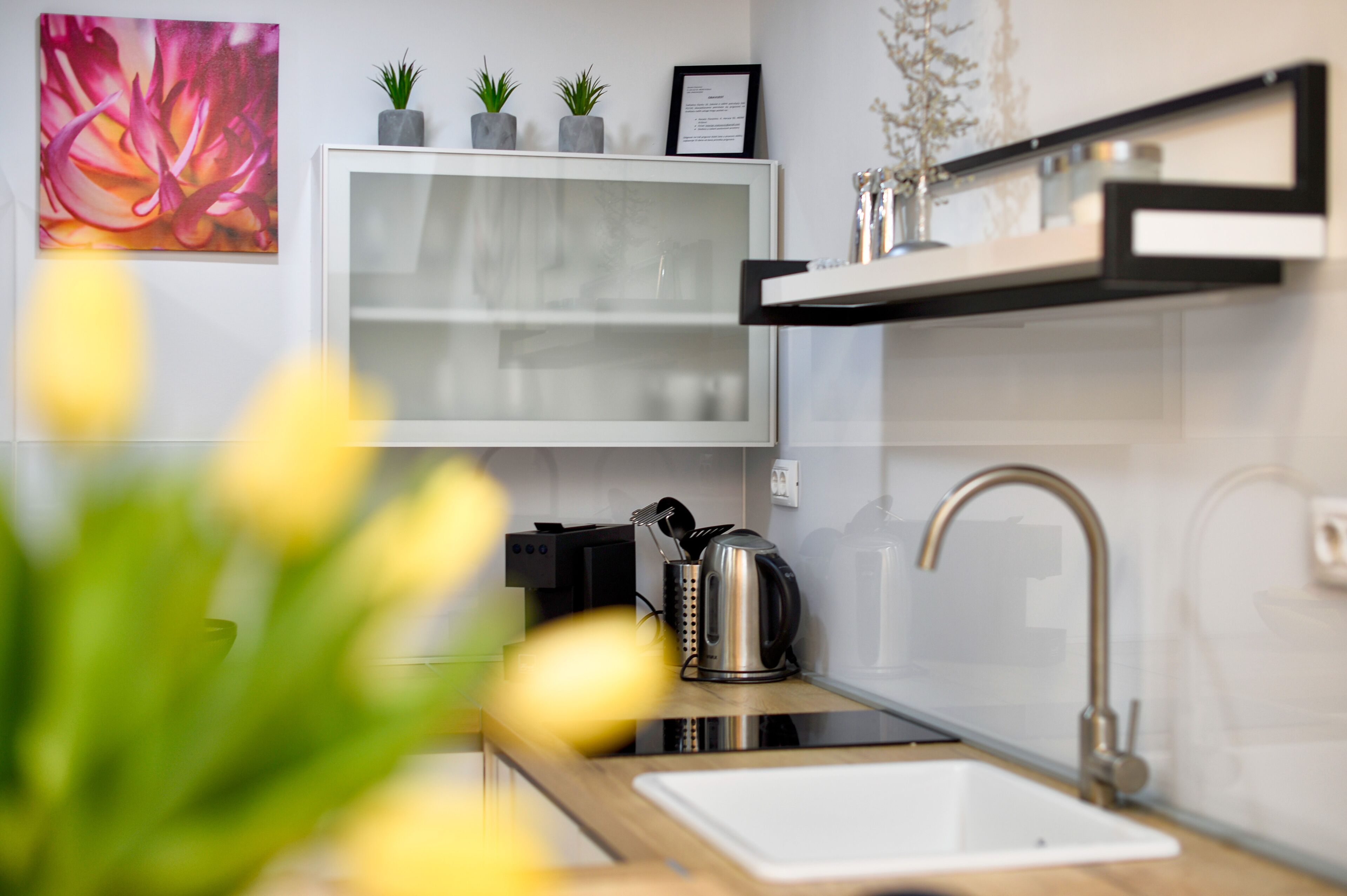 A modern kitchen with a white cabinet, a stainless steel kettle, and a sink.