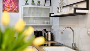 A modern kitchen with a white cabinet, a stainless steel kettle, and a sink.