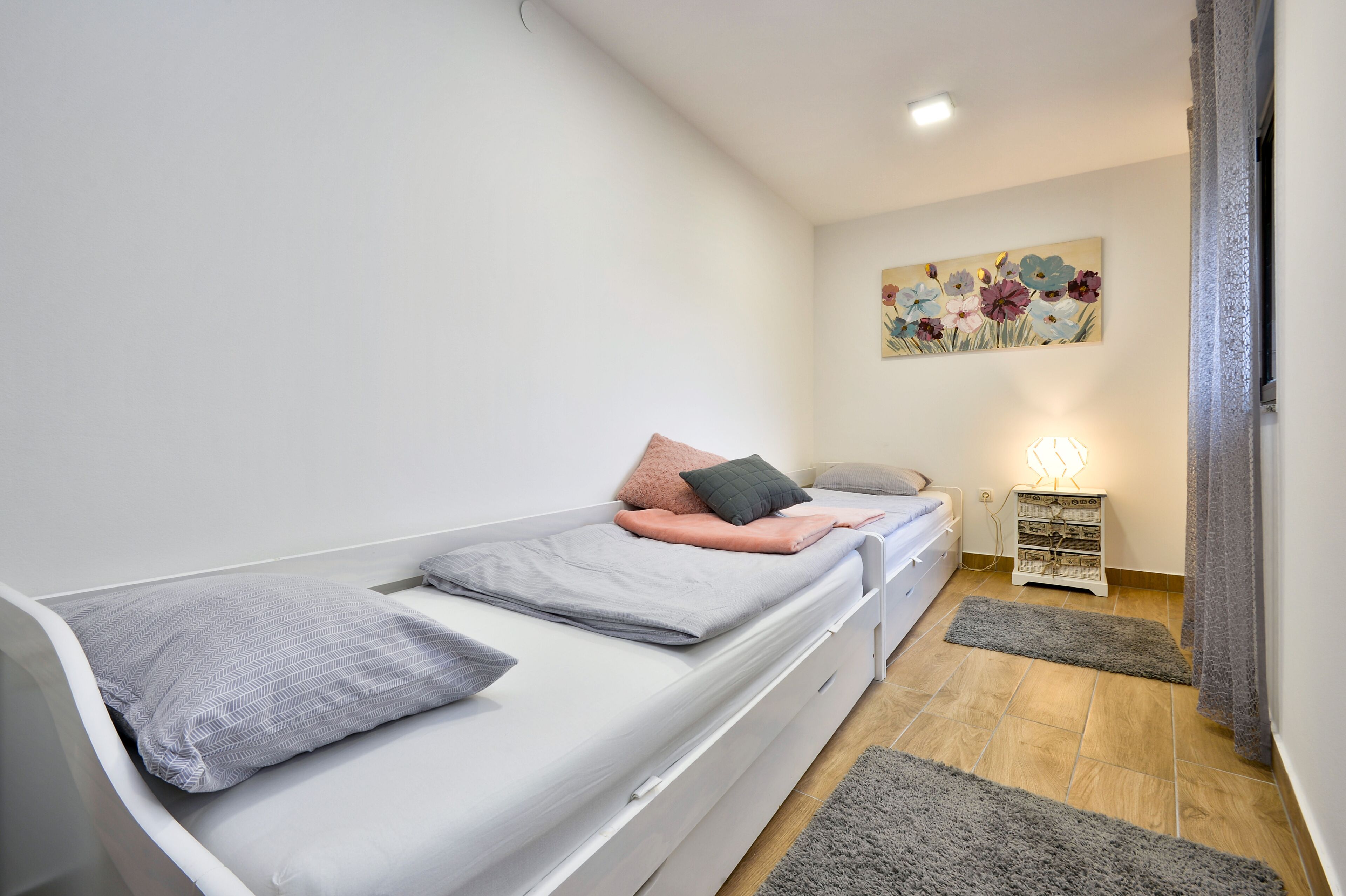 A modern bedroom with a single bed, a bedside table, a lamp, and a wall-mounted artwork.