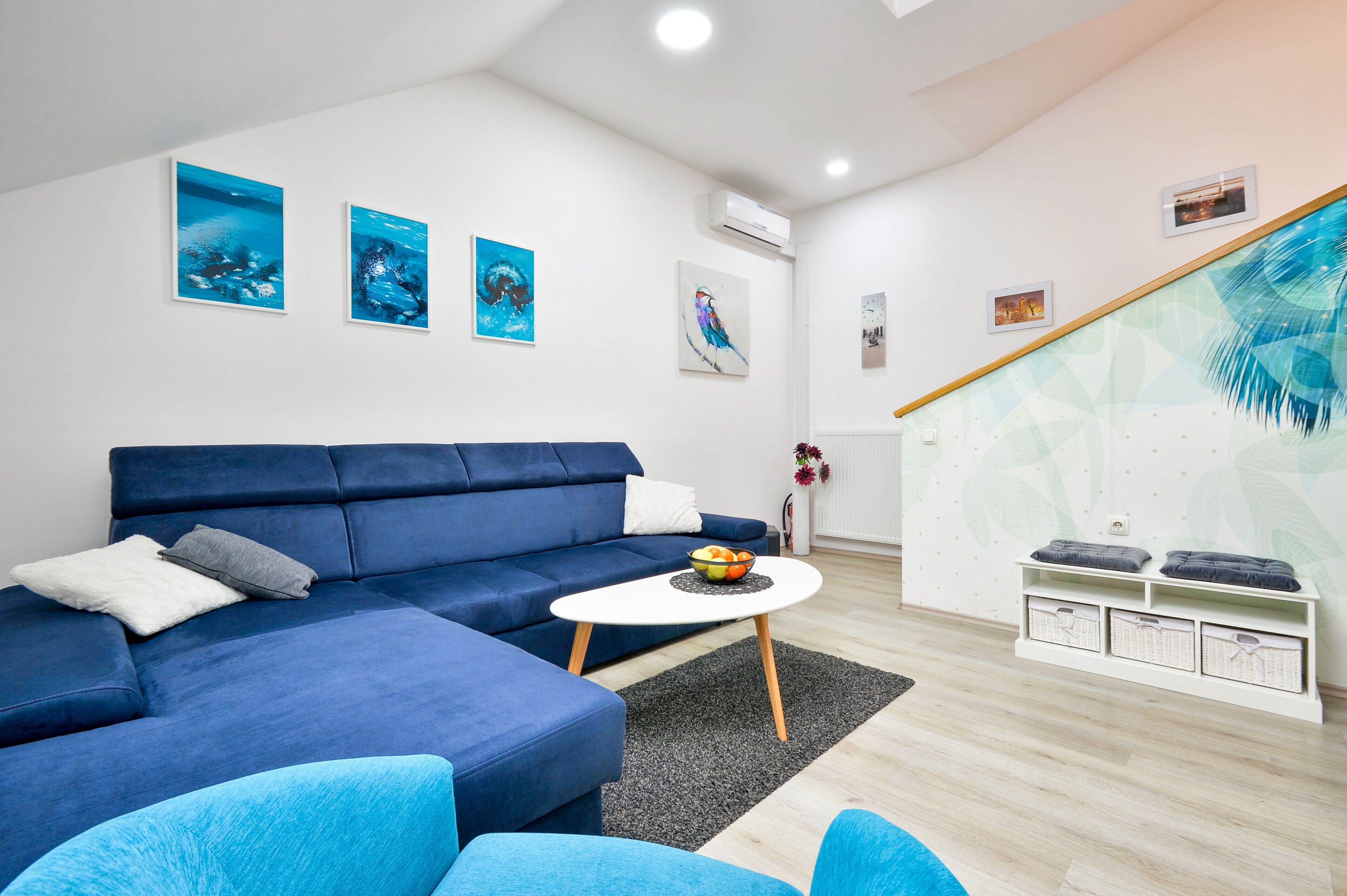 Un salon moderne avec un canapé bleu, une table basse blanche et des œuvres d’art accrochées aux murs.