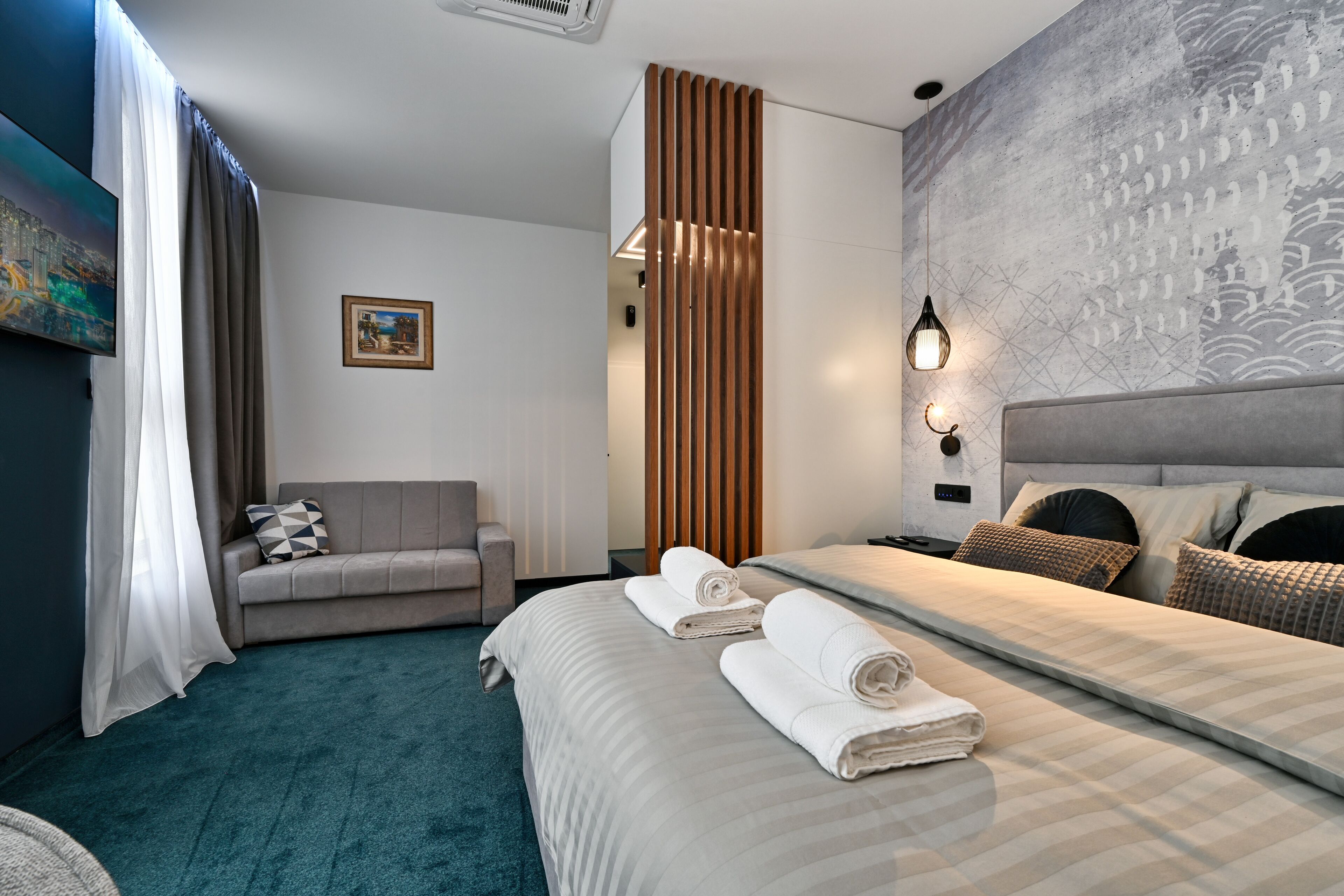 Una habitación de hotel con cama, sofá, un cuadro y pared con diseño texturizado.