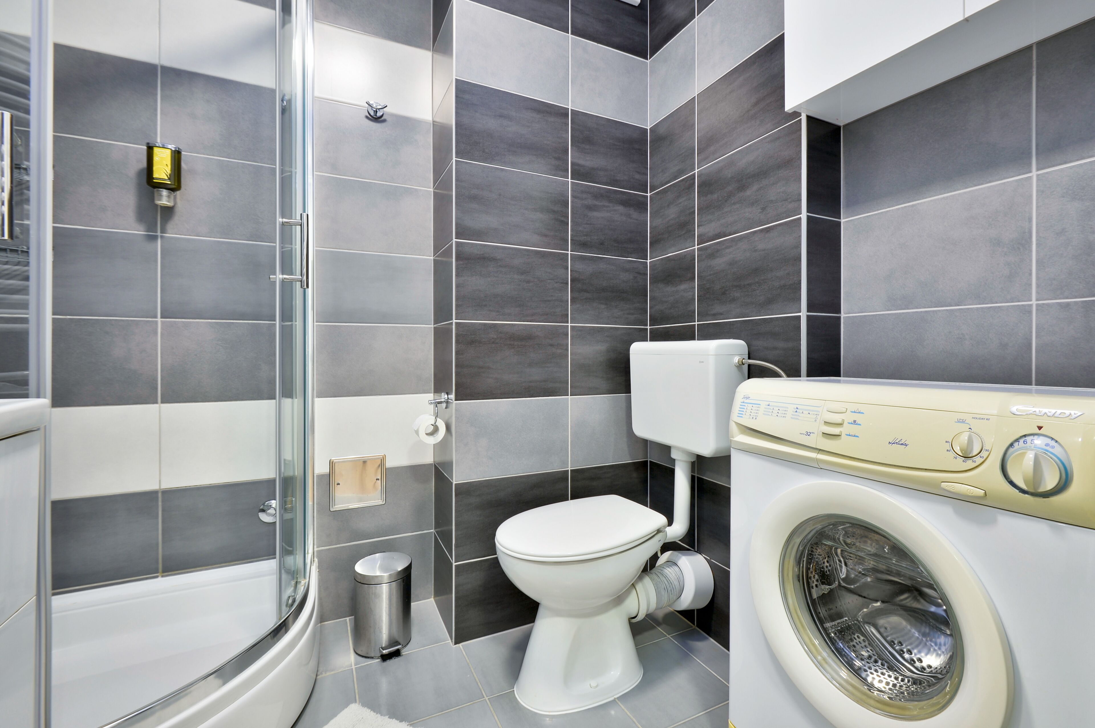 Un bagno moderno con box doccia in vetro, un water e una lavatrice a carica frontale.