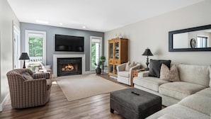 Een woonkamer met een open haard, een bank, een fauteuil en een kast.
