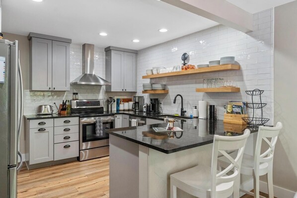 A modern kitchen with white cabinets, a stainless steel range hood, and a central island with bar stools.