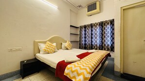 Un dormitorio ordenado con cama, mesita de noche, enchufe, aire acondicionado de pared y ventana con cortinas.