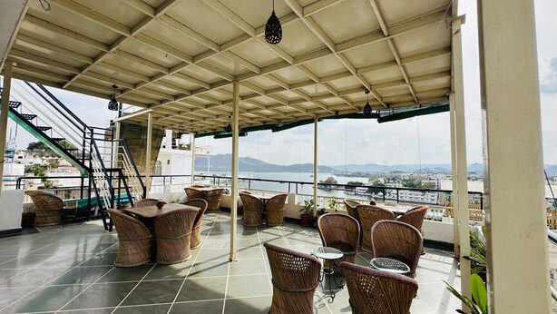 Una terraza techada con muebles de mimbre y vistas a un lago y montañas.