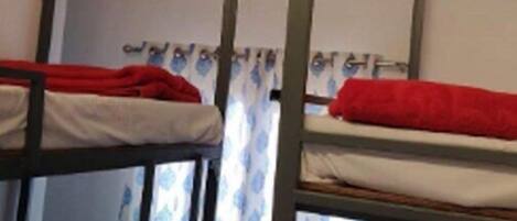 Dormitorio con literas, una ventana con cortinas y una lámpara en el techo.