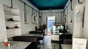 Interior de restaurante con suelo de baldosas blanco y negro, mesas y sillas, un ventilador de techo y un atril para el menú.