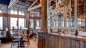 Un restaurante espacioso con techos altos, ventanas amplias y una zona de bar de madera.