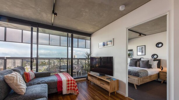 A modern living room with a large window, a flat-screen TV, a sofa, and a bed in the adjacent room. - Stylish 2-bed Apt in Southbank With Parking (Southbank)