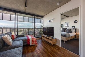 Una sala moderna con un ventanal grande, un televisor de pantalla plana, un sofá y una cama en la habitación contigua.